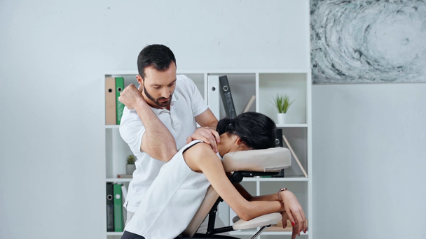handsome masseur making shoulders massage to businesswoman on massage chair - Materiaali, video