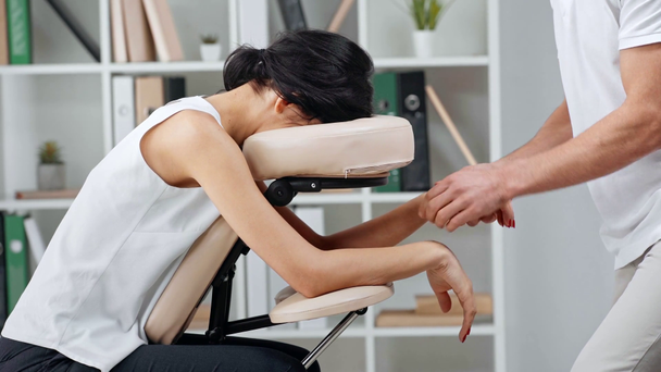 cropped view of masseur making hands massage to businesswoman on massage chair - Materiaali, video