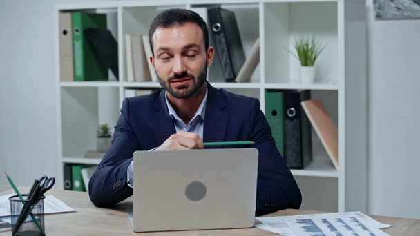 jóképű üzletember beszél közel laptop, miközben a kezében ceruza - Felvétel, videó