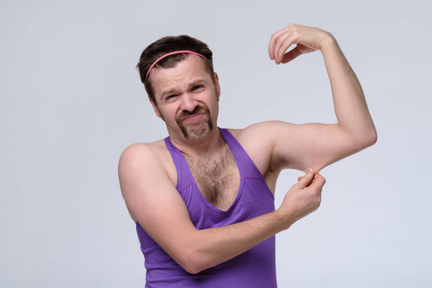 Grappige zwakke sportman oefenen kijken op zijn biceps. - Foto, afbeelding