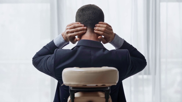 achteraanzicht van zakenman zittend in massage stoel en aanraken pijnlijke nek - Video