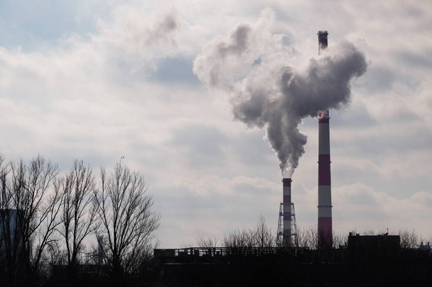 Industrielandschaft, Krakau, Polen: Weiß-rote Hochrohre der Anlage, aus denen Rauch oder Dampf auf dem Hintergrund grauweißer Wolken und des Himmels aufsteigt. Luftverschmutzung - Foto, Bild