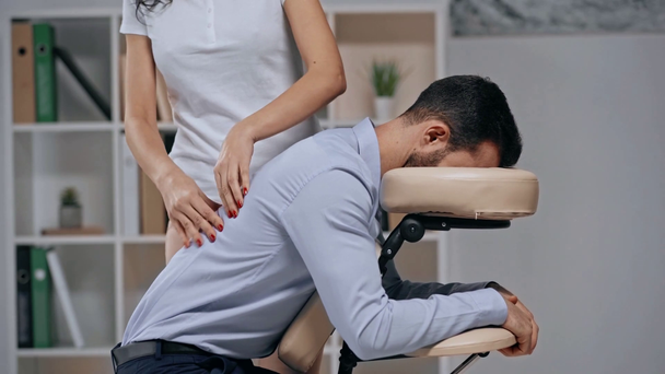 Teilansicht der Masseurin, die dem Geschäftsmann im Massagesessel Rückenmassage leistet - Filmmaterial, Video