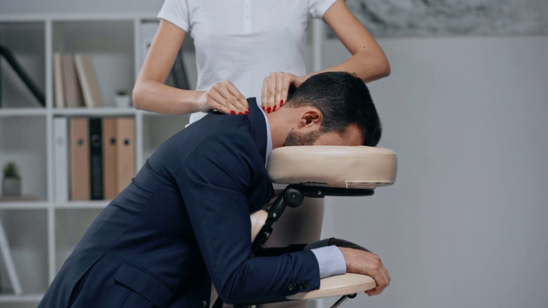 częściowy widok masażysty dokonywania masażu szyi do biznesmena na krześle do masażu - Materiał filmowy, wideo