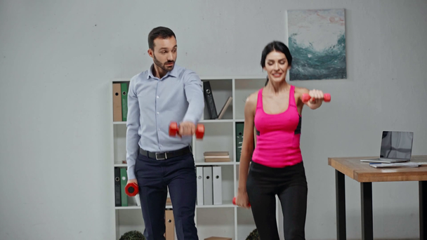 attractive fitness trainer and businessman exercising with dumbbells in office - Video, Çekim