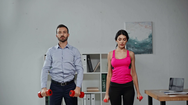 attractive fitness trainer and businessman exercising with dumbbells in office - Footage, Video