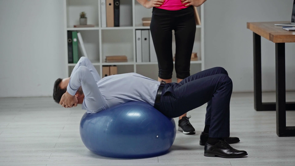 bijgesneden weergave van fitness trainer in de buurt van zakenman doet buikspieren op fitness bal - Video