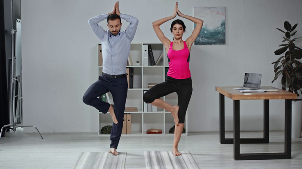 mooie yoga instructeur en knappe zakenman staande in meditatie poses  - Video