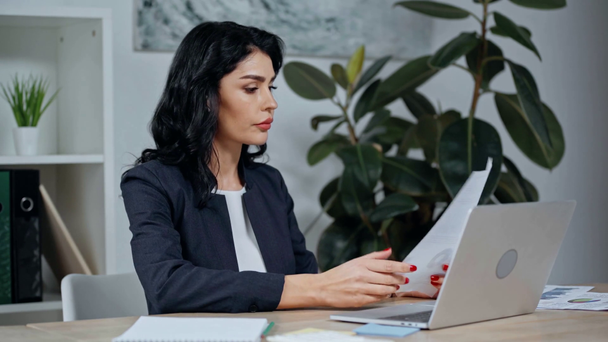 attractive businesswoman typing on laptop while sitting at workplace - Video, Çekim