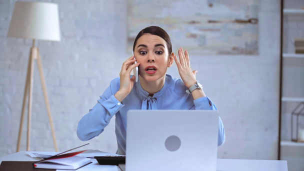 mujer de negocios enojado hablando en el teléfono inteligente cerca del ordenador portátil
  - Metraje, vídeo