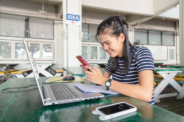 Las mujeres asiáticas están trabajando con el teléfono móvil y portátil sobre la mesa en el área universitaria. Se ve feliz por el trabajo. concepto de adicto a las redes sociales
. - Foto, imagen