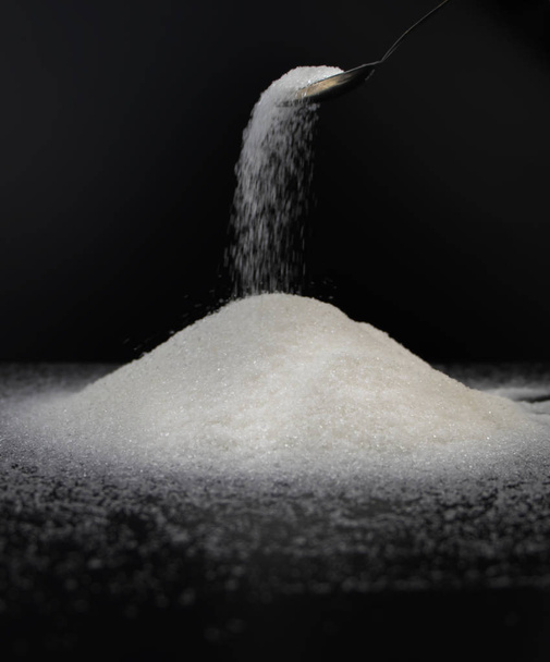 Spoon in sugar on a black background. The concept of addiction to sweets. Macro photo of granulated sugar. - Foto, Imagem