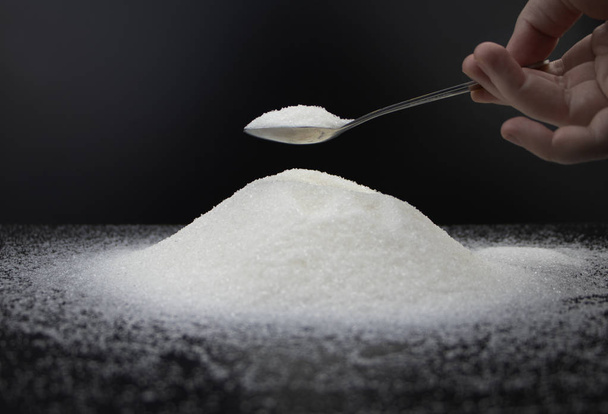 Spoon in sugar on a black background. The concept of addiction to sweets. Macro photo of granulated sugar. - Photo, Image