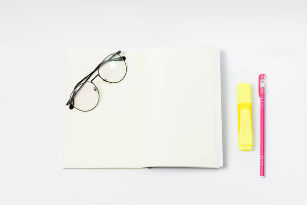 Kırtasiye malzemeleri ya da Gözlük İşaretleyici olarak çalışma ve beyaz arka planda orta konuma sahip boş bir defter üzerinde kalem. Okul konseptine geri dönelim. çalışma konsepti. - Fotoğraf, Görsel