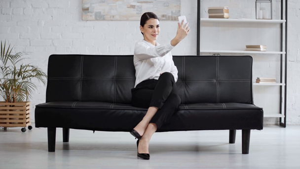 happy businesswoman taking selfie and sitting on sofa - Materiał filmowy, wideo