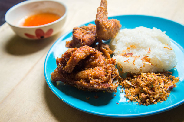 Жареная курица и жареный лук с липким рисом и соусом в светло-голубом блюде на коричневом дереве. жареная курица самая знаменитая еда в Таиланде Hat-yai Songkhla. Культурная еда. Жирная пища
. - Фото, изображение