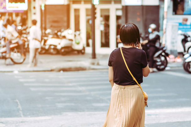 Asyalı bir kadının arka görüntüsü şehir merkezinde yaya geçidinde yürürken telefonu kullanıyor.. - Fotoğraf, Görsel