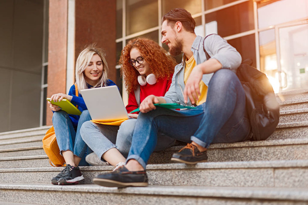Cheerful students sitting on stairs and using laptop - Photo, Image
