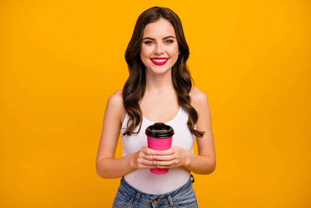 Photo of funny pretty lady hold pink paper takeout coffee cup hot beverage spend free time leisure rejoicing wear white tank-top jeans isolated bright yellow color background - Foto, Imagem