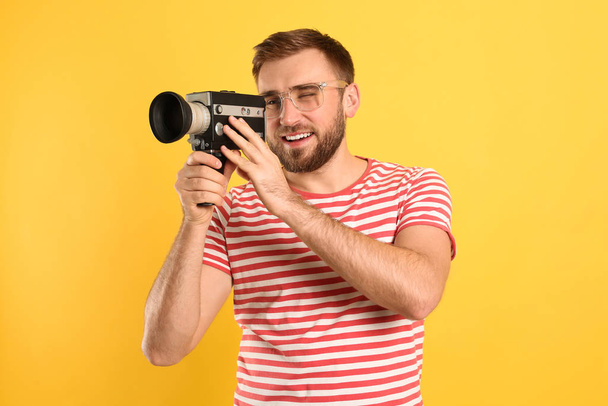 Young man using vintage video camera on yellow background - Фото, зображення
