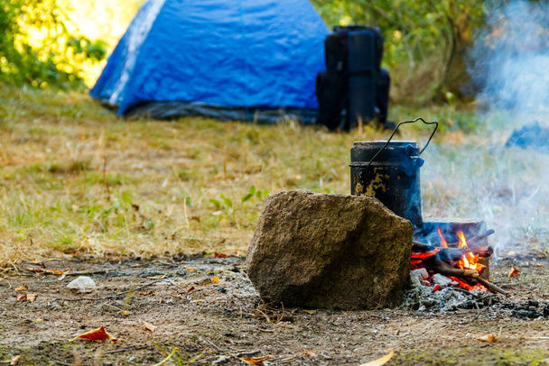 Cuisiner sur le feu de camp dans le camping. Tente et sac à dos sur fond
 - Photo, image