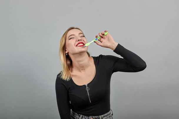 Young blonde girl in black jacket happy woman brushing her teeth - Photo, Image
