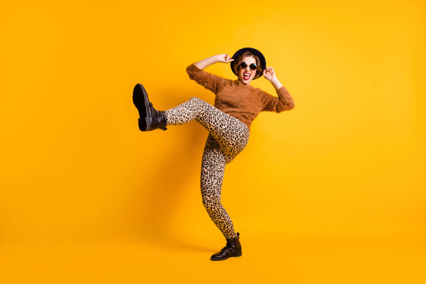 Full size photo of funky lady raise leg high rejoice vacation abroad student youth party excited mood wear soft sweater leopard pants specs retro cap boots isolated yellow color background - 写真・画像