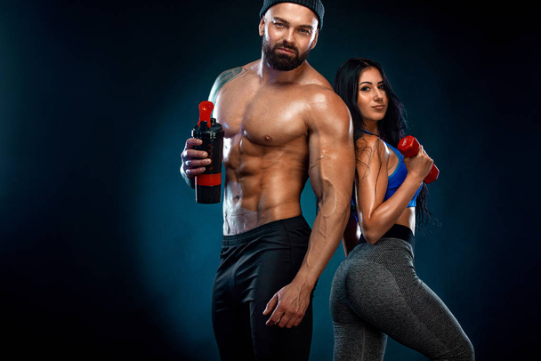 Athletic couple. Man and fit woman with sports equipment on dark background. - Фото, изображение