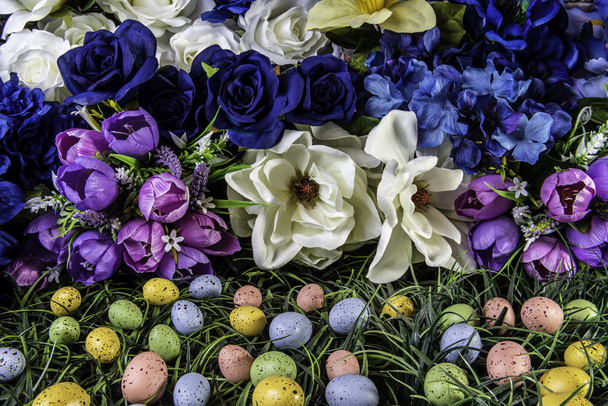 small colored Easter eggs in green grass with colorful spring flowers for background - Foto, afbeelding
