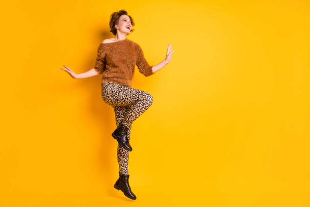 Full body photo of amazing funky lady jumping up high youth trend look rejoicing weekend vacation wear fluffy sweater leopard pants shoes isolated yellow color background - Photo, image