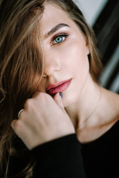 Portrait of a beautiful girl with light brown long hair in a black t-shirt and jeans on the stairs in the house. Beautiful blue eyes - Фото, зображення