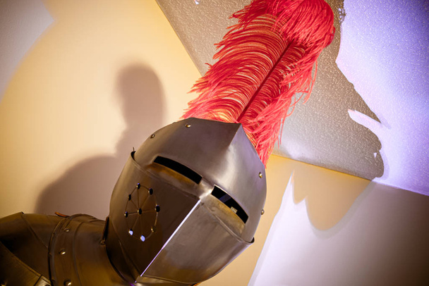 Un traje de armadura en un centro de atención en una habitación blanca con gorra de plumas rojas
 - Foto, Imagen