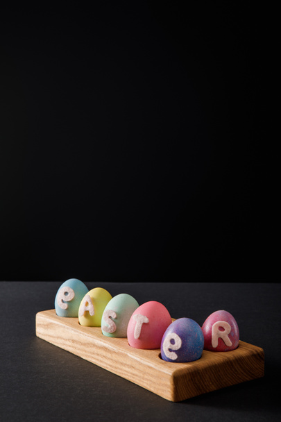 Painted chicken eggs with easter lettering on wooden board on grey and black background - Foto, Bild