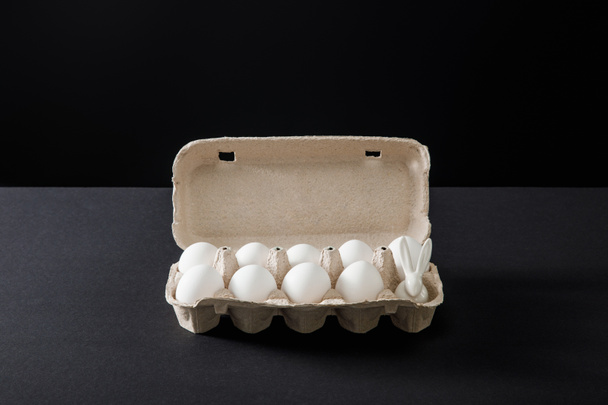 Egg tray with chicken eggs and decorative bunny on grey and black background - Foto, Bild
