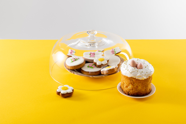 Bowl with tasty cookies covered by glass lid near easter cake isolated on grey background - Fotografie, Obrázek