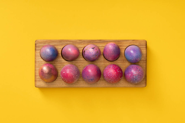 Vista superior de tablero de madera con coloridos huevos de Pascua sobre fondo amarillo
 - Foto, Imagen