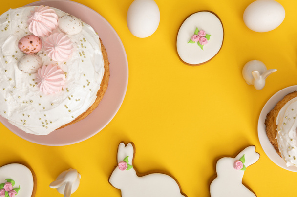 Top view of easter cakes with chicken eggs, cookies and decorative bunnies on yellow background - Φωτογραφία, εικόνα