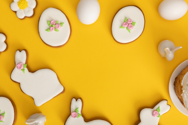 Top view of chicken eggs, cookies and decorative bunnies on yellow background - Photo, Image