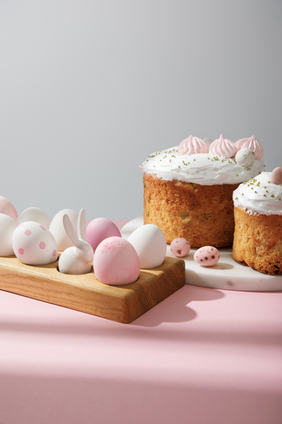 Huevos de Pascua sobre tabla de madera con conejo decorativo con pasteles de Pascua en rosa y gris
  - Foto, imagen