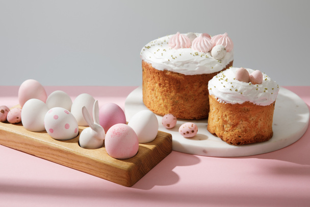 Easter eggs on wooden board with decorative bunny near easter cakes on pink and grey  - Foto, immagini