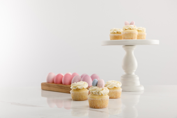 Focus selettivo di deliziosi cupcake pasquali su supporto di superficie e torta e uova di pollo dipinte su sfondo grigio
  - Foto, immagini
