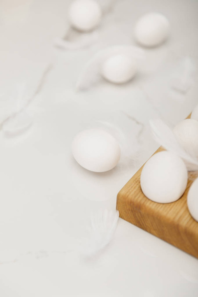 Selective focus of eggs on wooden egg tray and feathers on white background - Photo, Image