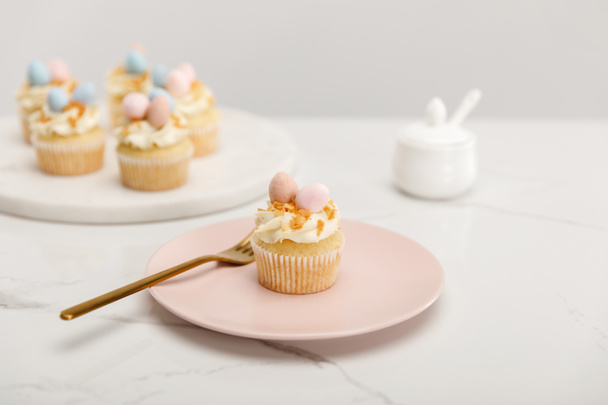 Selective focus of cupcakes on plate with fork and round board with sugar bowl on grey background - Foto, Imagen