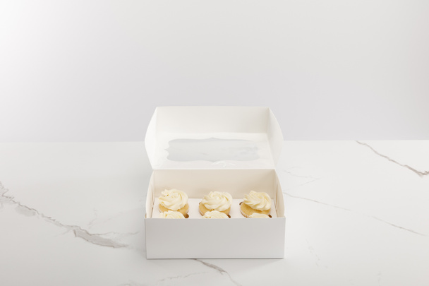 Tasty cupcakes in box isolated on grey - 写真・画像