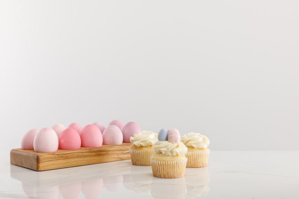 Easter eggs on egg tray with delicious cupcakes isolated on grey background - 写真・画像