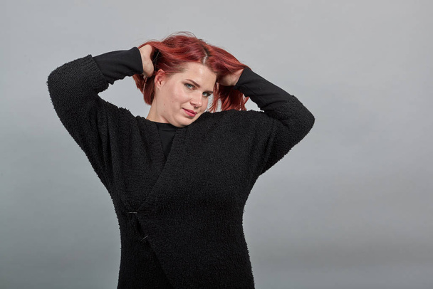 rousse fille en pull noir grosse femme joue avec ses cheveux, ajuste la coiffure
 - Photo, image