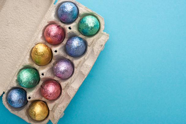 Top view of chocolate easter eggs in egg tray on blue background - 写真・画像