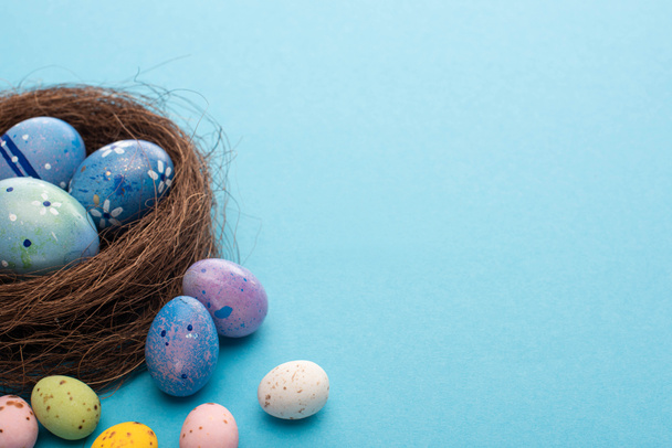 Nest and colorful chicken and quail eggs on blue background - Photo, Image