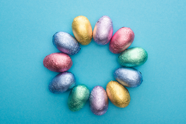 Вид зверху на коло з шоколадом Великодні яйця в барвистій фользі на синьому фоні
 - Фото, зображення