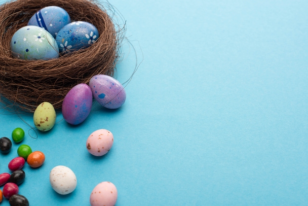 Nest with Easter eggs and colorful candies on blue background - Foto, Imagem